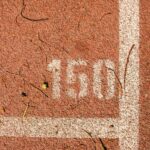 Close-up of a running track showing the number 150 marked on red surface with white lines.